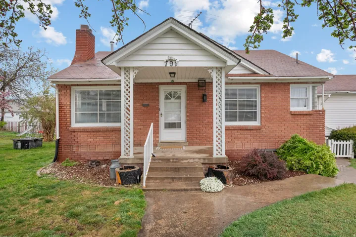 View of front of property with brick siding, a chimney, and a shingled roof