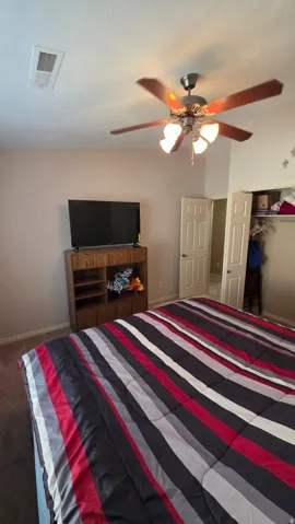 Bedroom with a closet, ceiling fan, and dark colored carpet