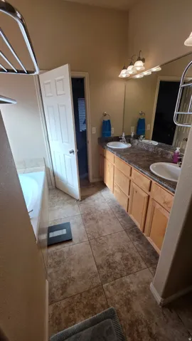 Full bathroom featuring a garden tub, double vanity, and light tile patterned floors