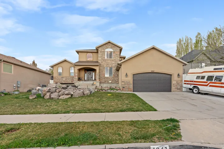 View of front of property featuring stucco siding, concrete driveway, stone siding, an attached garage, and a front lawn