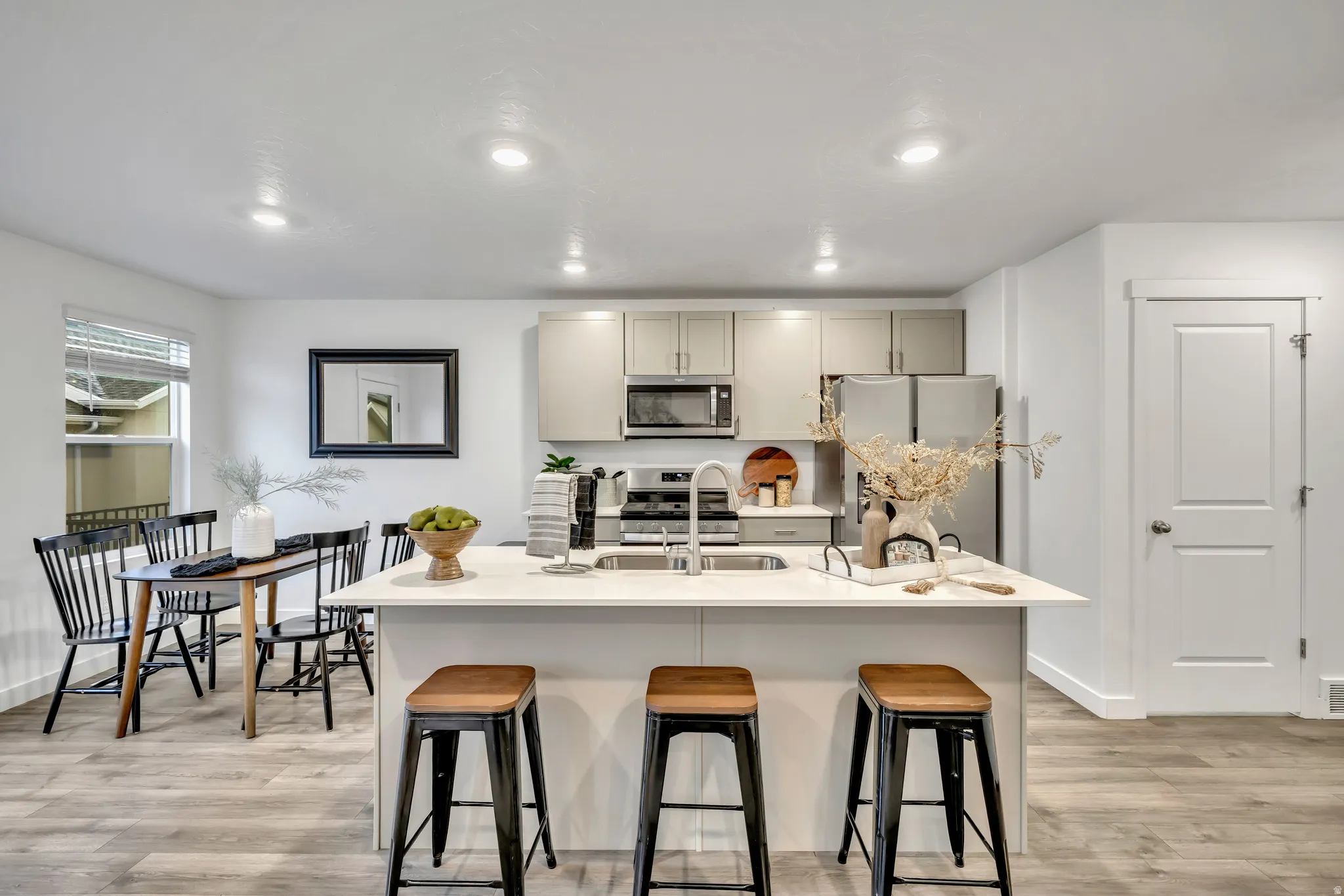 Kitchen featuring stainless steel appliances, light wood-style flooring, a kitchen bar, an island with sink, and recessed lighting