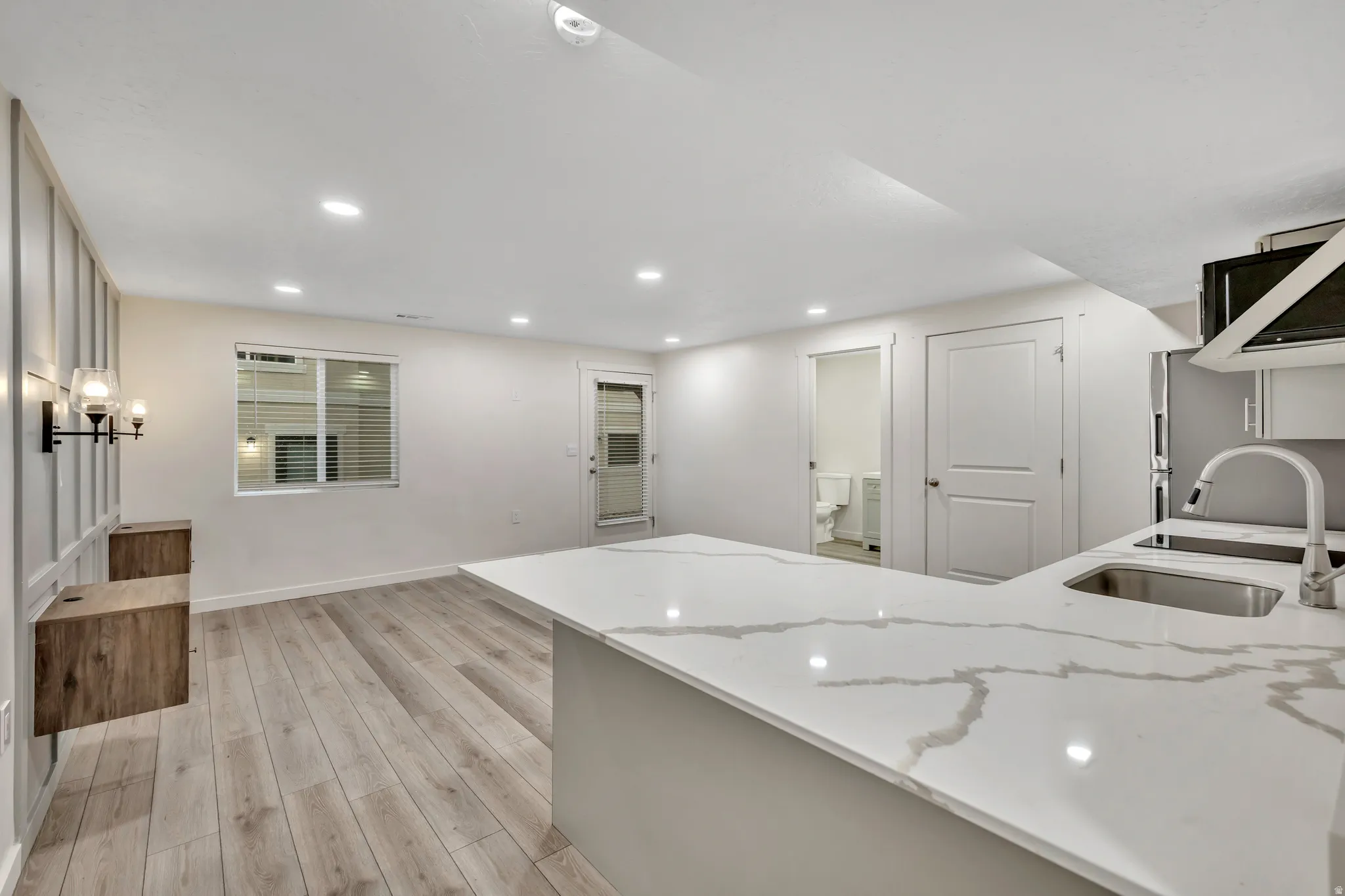 Basement studio featuring light quartz countertops, light wood-style LVP flooring, recessed lighting, freestanding refrigerator, and a peninsula