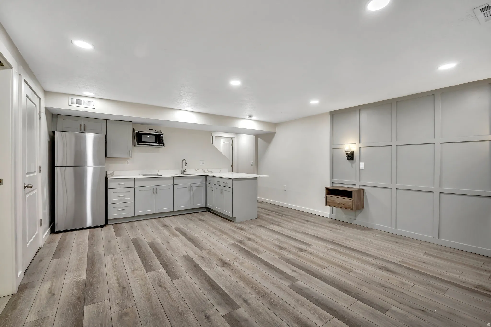 Basement studio featuring gray cabinetry, light countertops, freestanding refrigerator, a decorative wall, and light wood-type flooring