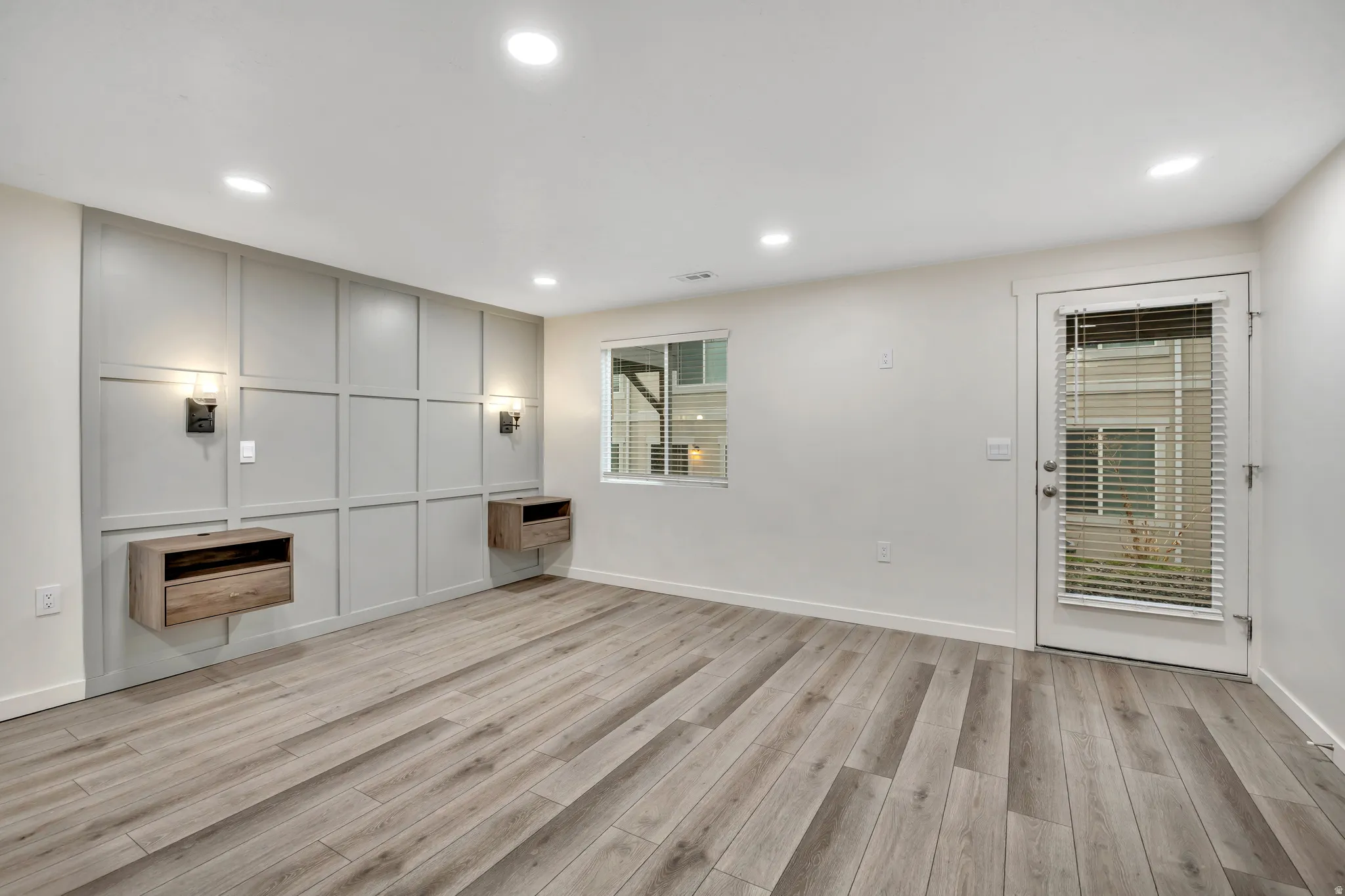 Basement studio living area featuring light wood-style floors, recessed lighting, and a decorative wall