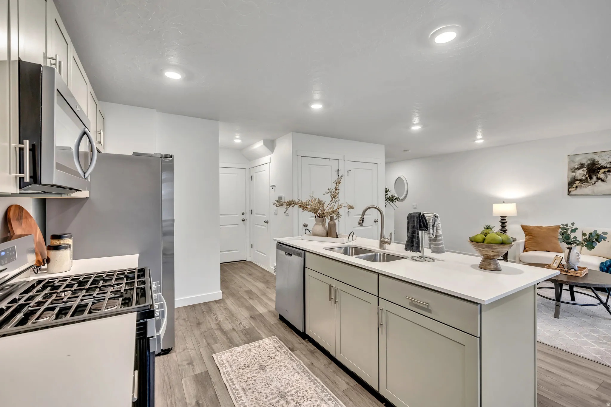 Kitchen featuring stainless steel appliances, a center island with sink, light wood finished floors, open floor plan, and light stone counters