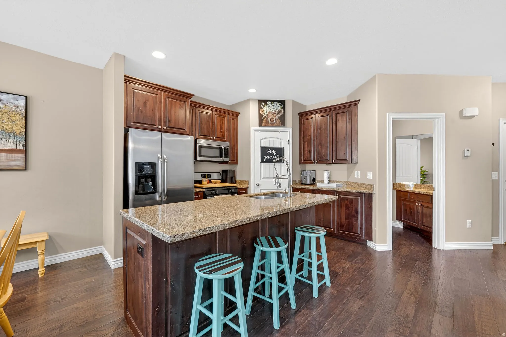 Kitchen with stainless steel appliances, dark wood-type flooring, light stone countertops, a kitchen island with sink, and recessed lighting