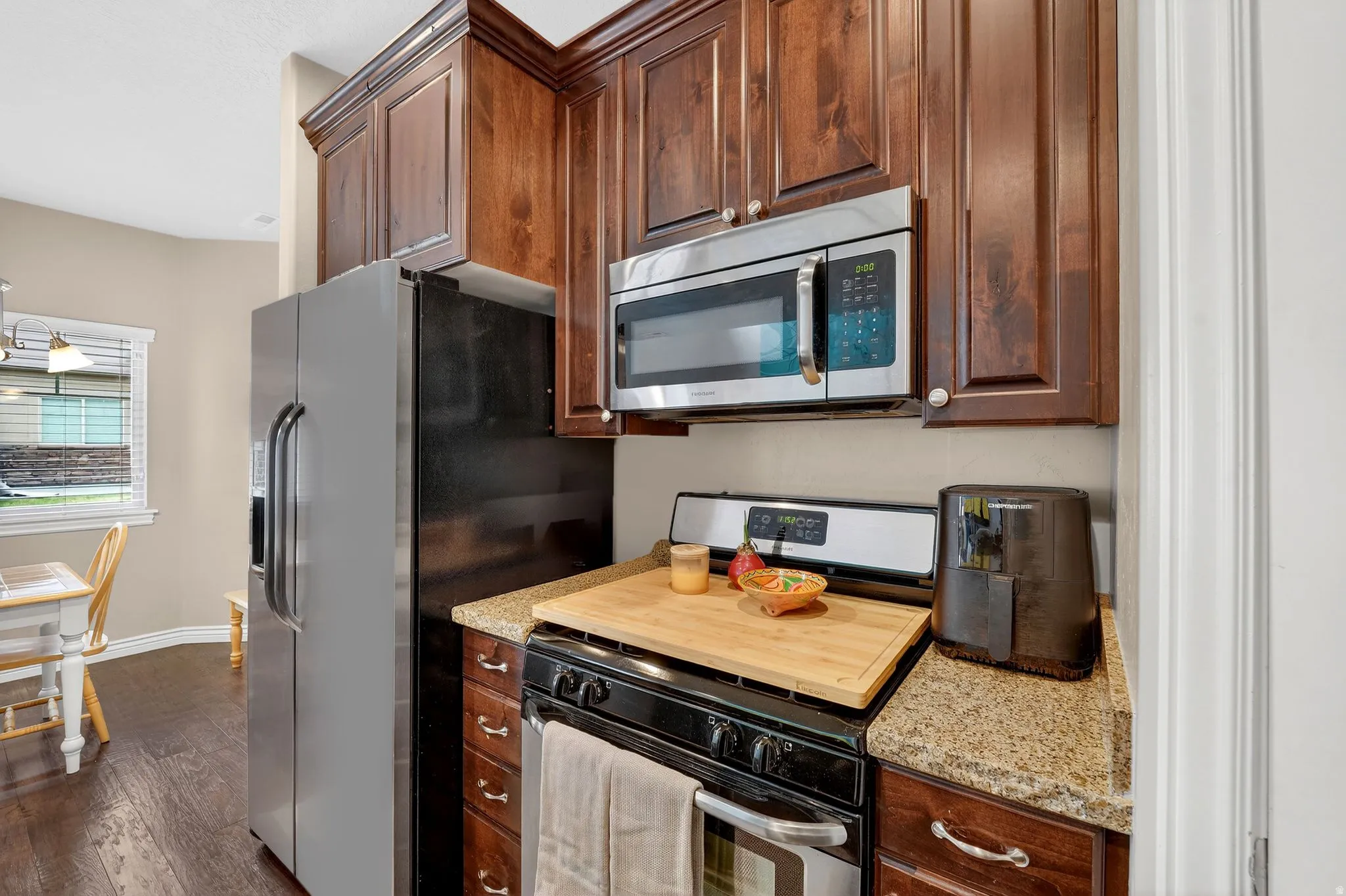 Kitchen featuring stainless steel appliances, light stone countertops, dark wood-style floors, and dark wood finish cabinetry