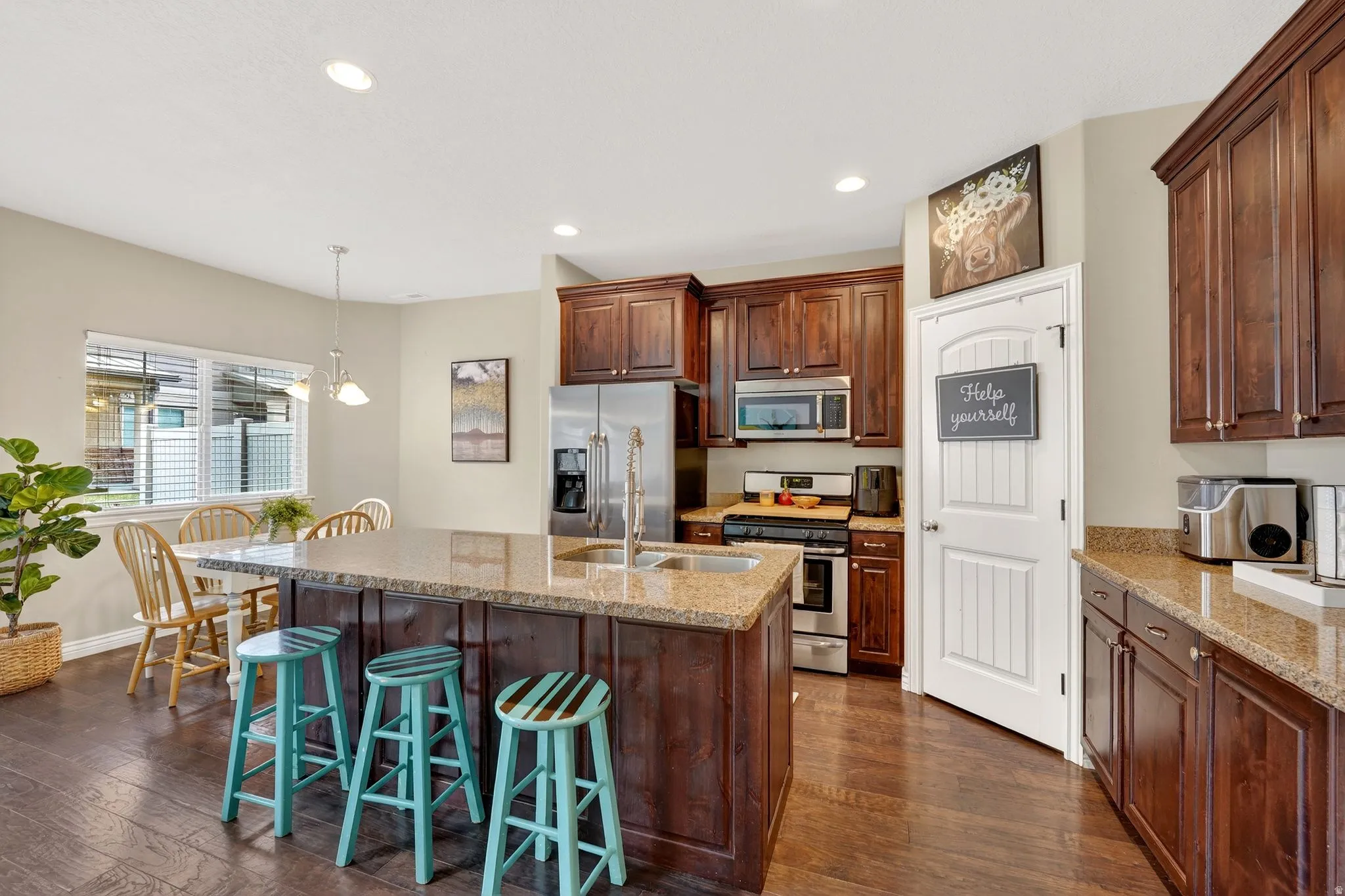Kitchen with stainless steel appliances, an island with sink, dark wood-type flooring, and light stone countertops