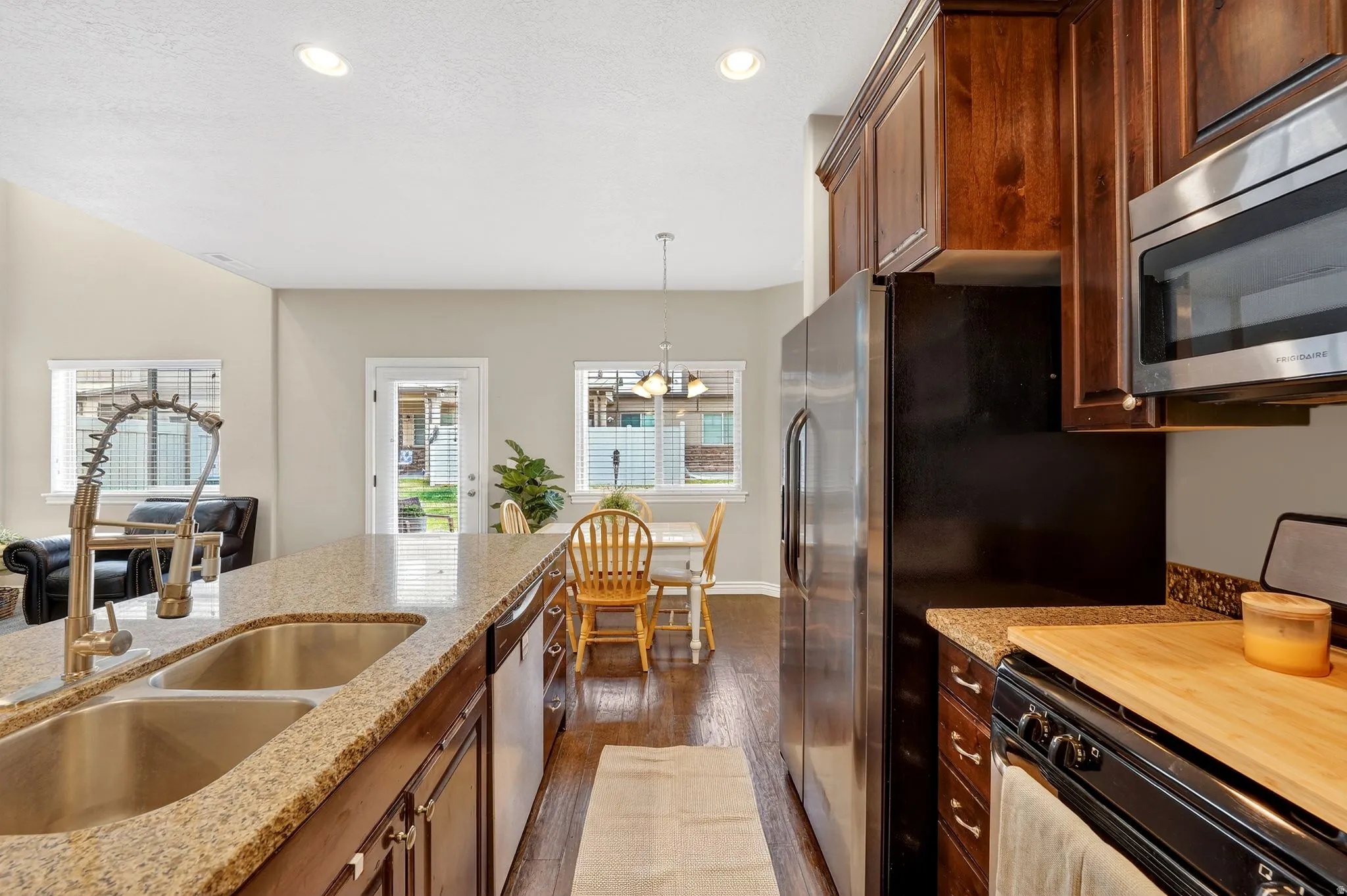 Kitchen featuring stainless steel appliances, dark wood-style floors, pendant lighting, light stone counters, and wood finish cabinetry