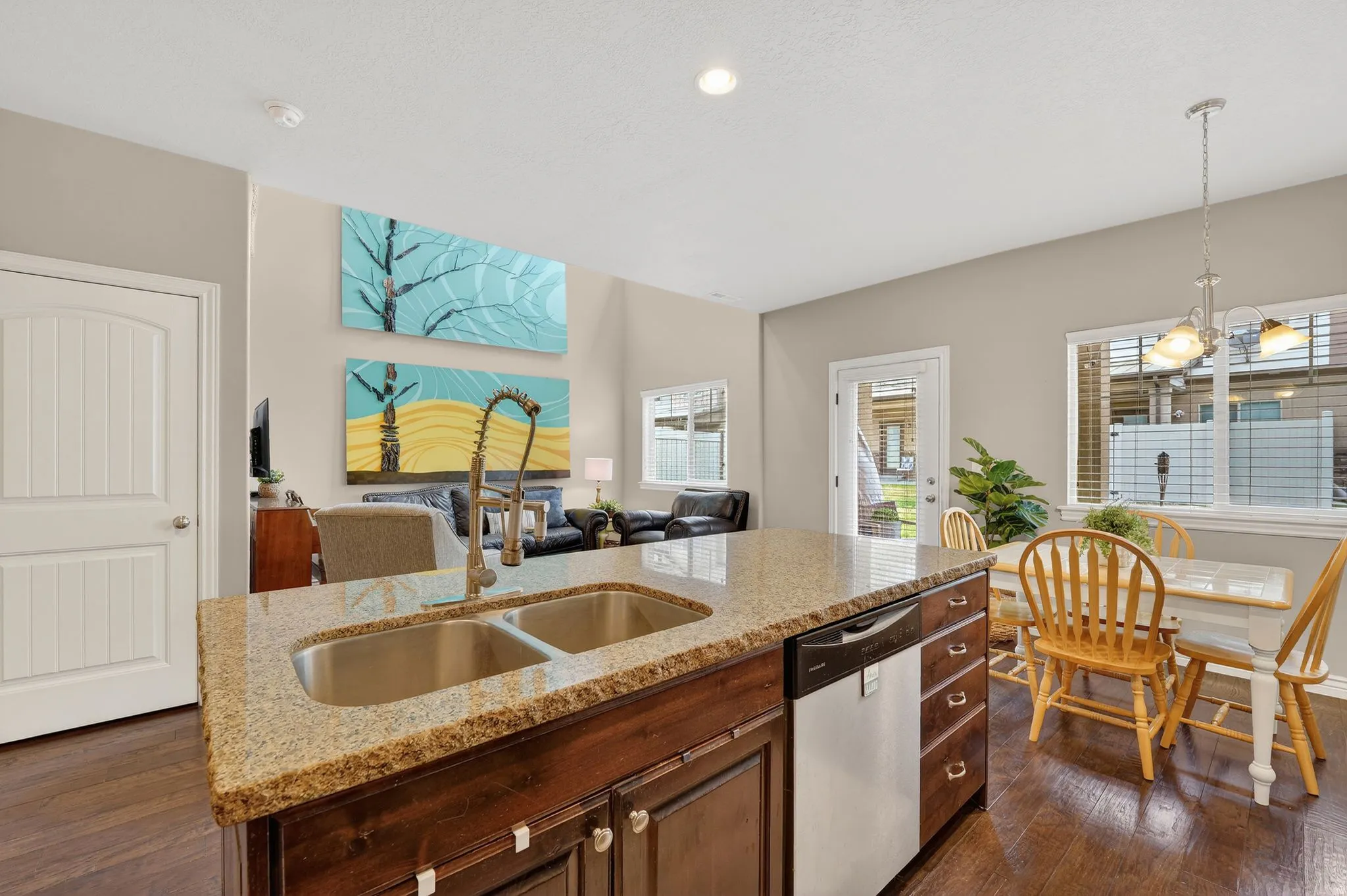 Kitchen with open floor plan, dishwasher, light stone counters, a kitchen island with sink, and dark wood-style flooring