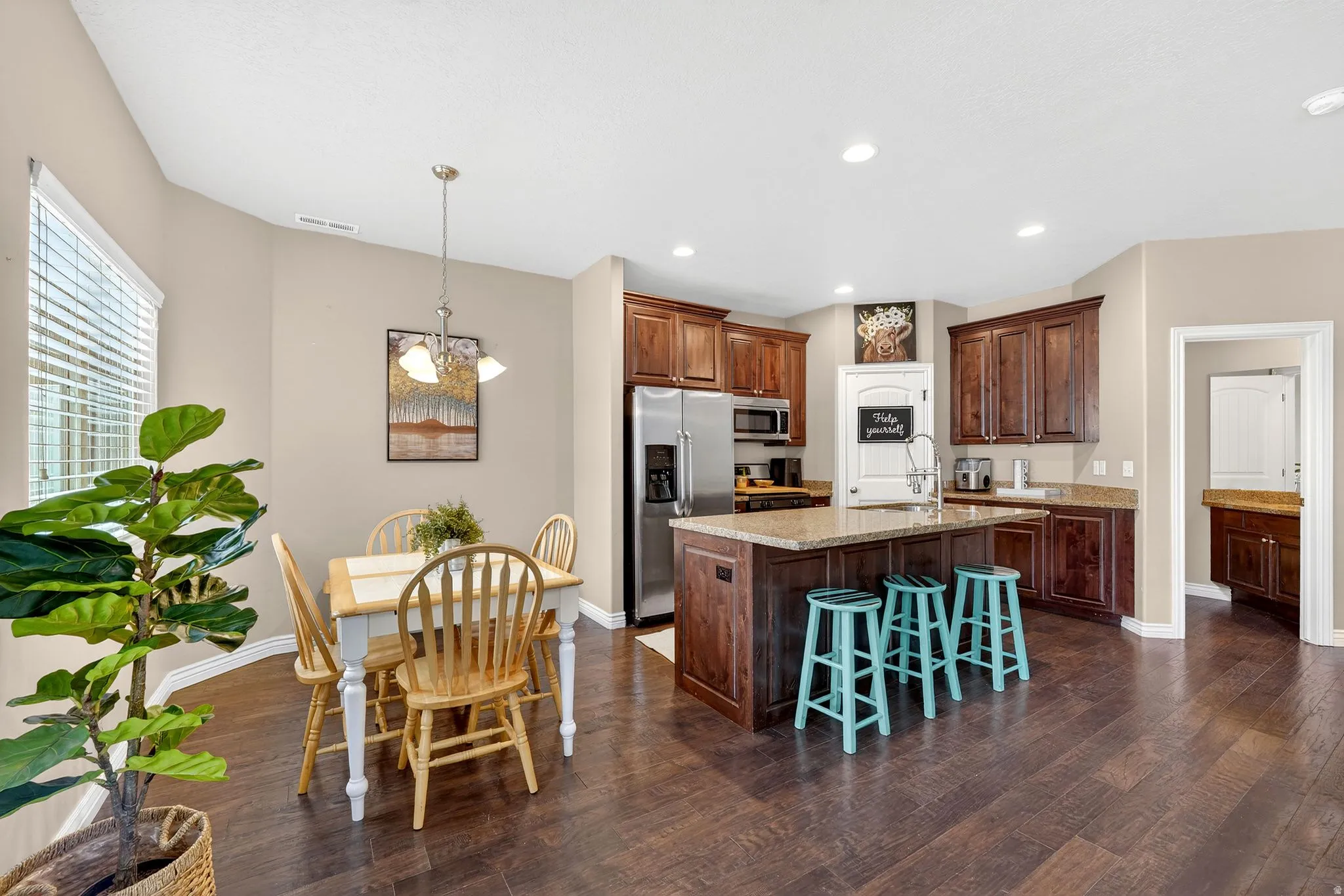 Kitchen with stainless steel appliances, light stone countertops, a breakfast bar area, an island with sink, and dark wood-style floors