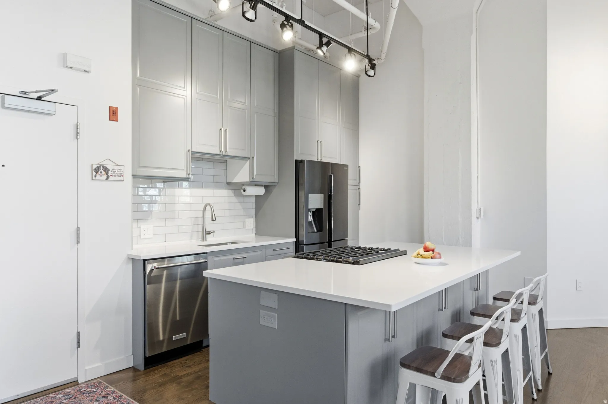 Kitchen featuring gray cabinetry, decorative backsplash, stainless steel appliances, dark wood finished floors, and a center island