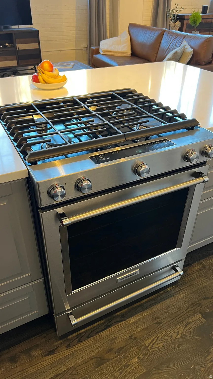 Kitchen view of stainless steel range with gas stovetop, dark wood-style floors, gray cabinets, and light stone countertops
