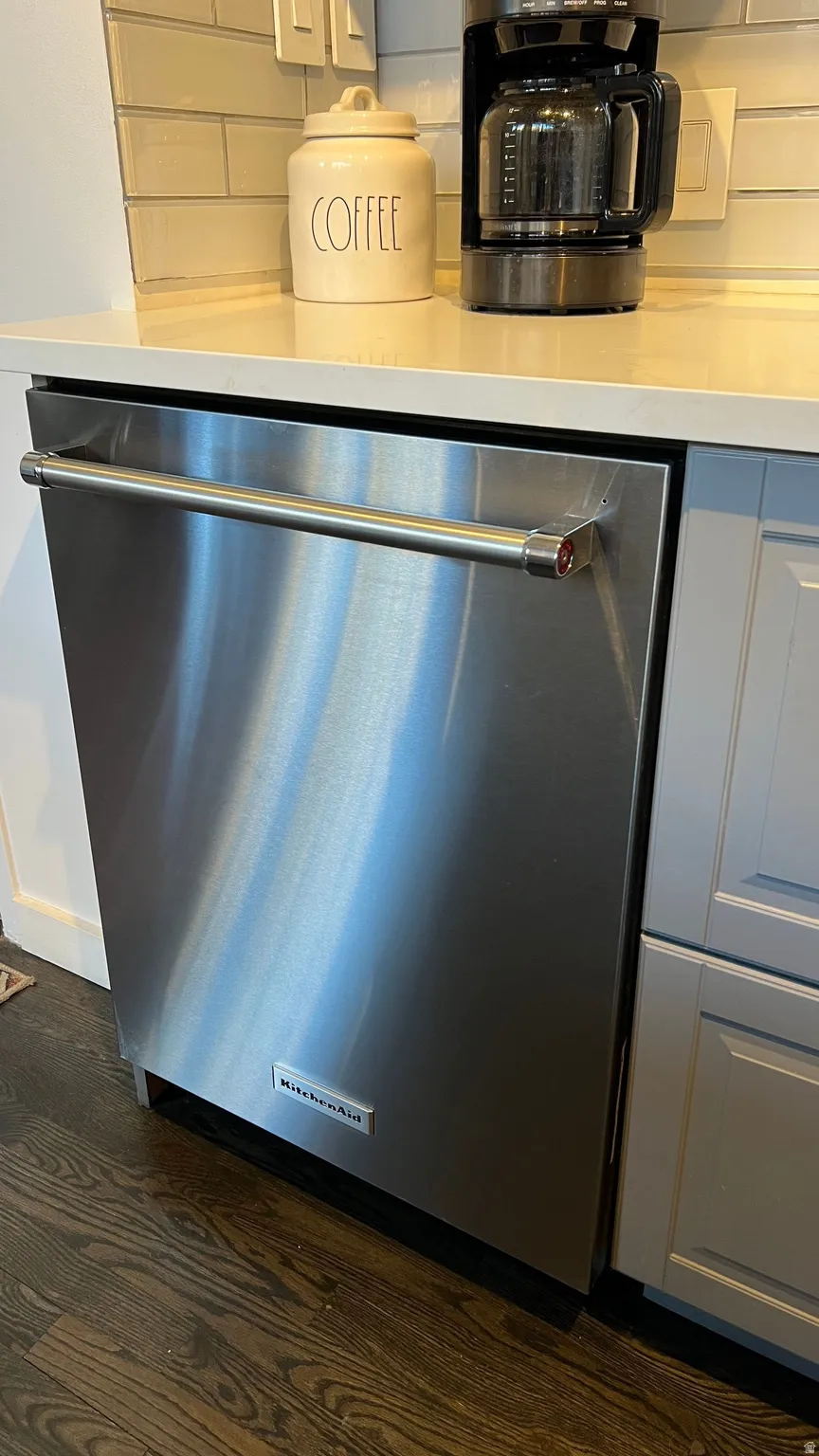 Kitchen view of dishwasher, tasteful backsplash, dark wood-type flooring, and white cabinets