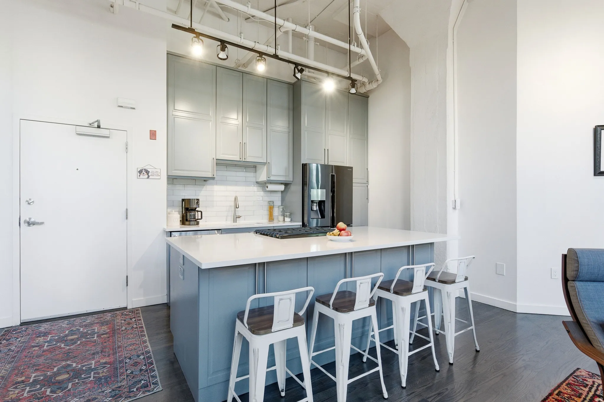 Kitchen with gray cabinetry, a breakfast bar area, stainless steel fridge, tasteful backsplash, and a high ceiling