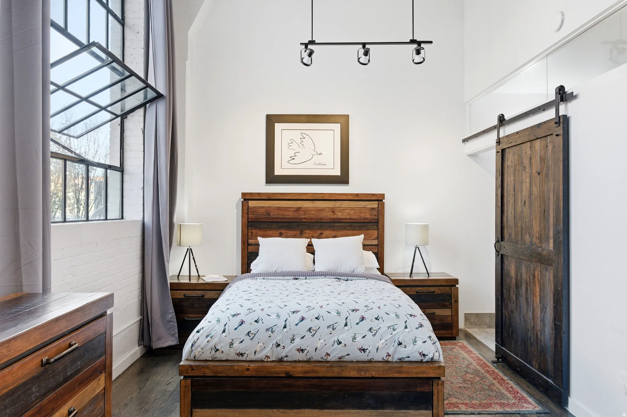 Bedroom featuring a barn door, multiple windows, and dark wood-style flooring