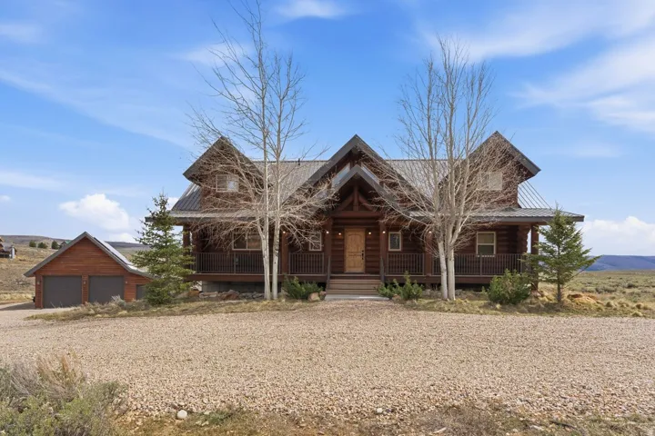 Log cabin featuring a porch, a garage, driveway, and a metal roof