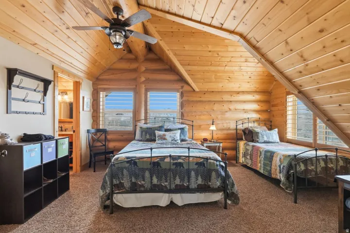 Carpeted bedroom with log walls, wooden ceiling, lofted ceiling with beams, and ceiling fan