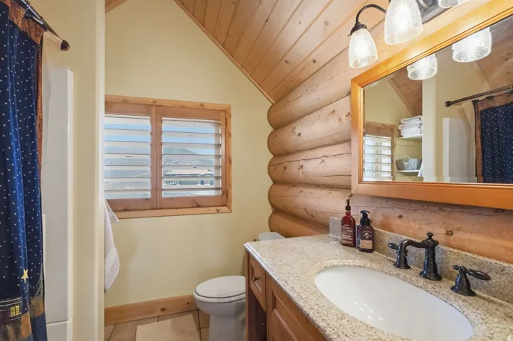 Bathroom with a shower with shower curtain, rustic walls, vanity, a vaulted wooden ceiling, and light tile patterned floors