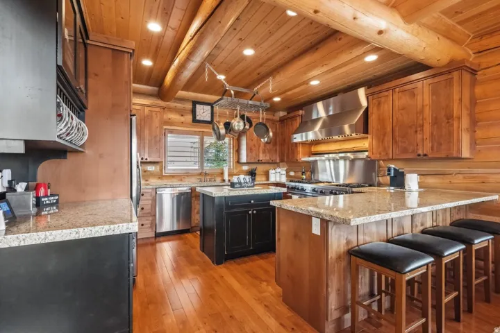 Kitchen featuring beamed ceiling, light wood finished floors, a peninsula, stainless steel appliances, and a kitchen bar