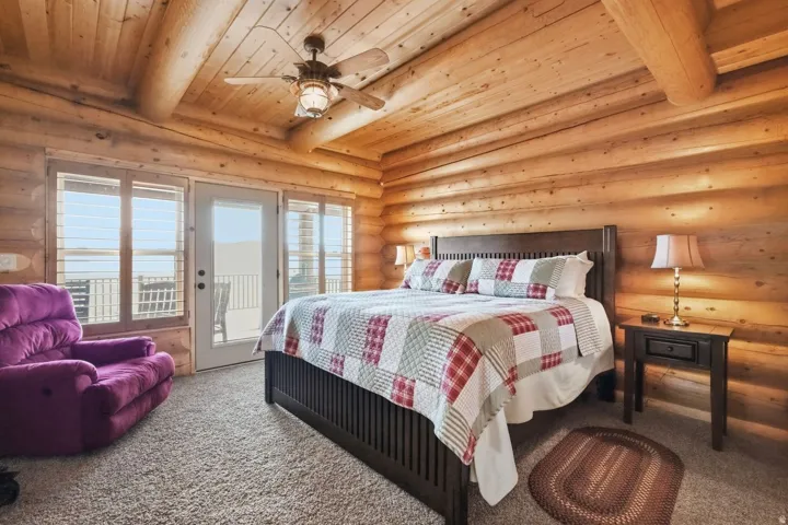Bedroom featuring rustic walls, carpet, access to outside, a wooden ceiling with exposed beams, and a ceiling fan