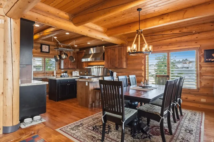Dining space featuring a chandelier, dark wood-type flooring, a wood ceiling with exposed beams, and log walls