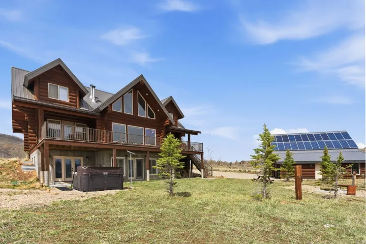 Rear view of house featuring a hot tub, log exterior, a lawn, solar panels, and a patio