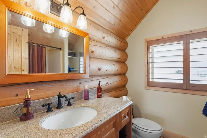 Full bath with a shower with shower curtain, log walls, vanity, and a vaulted wood ceiling