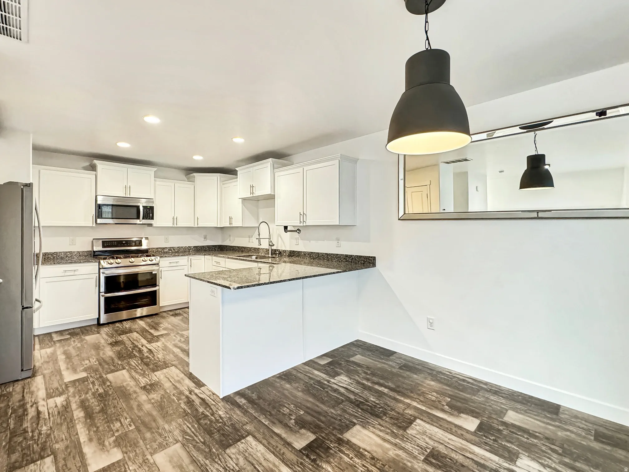 Kitchen featuring stainless steel appliances, a peninsula, white cabinetry, dark wood-style floors, and dark stone counters