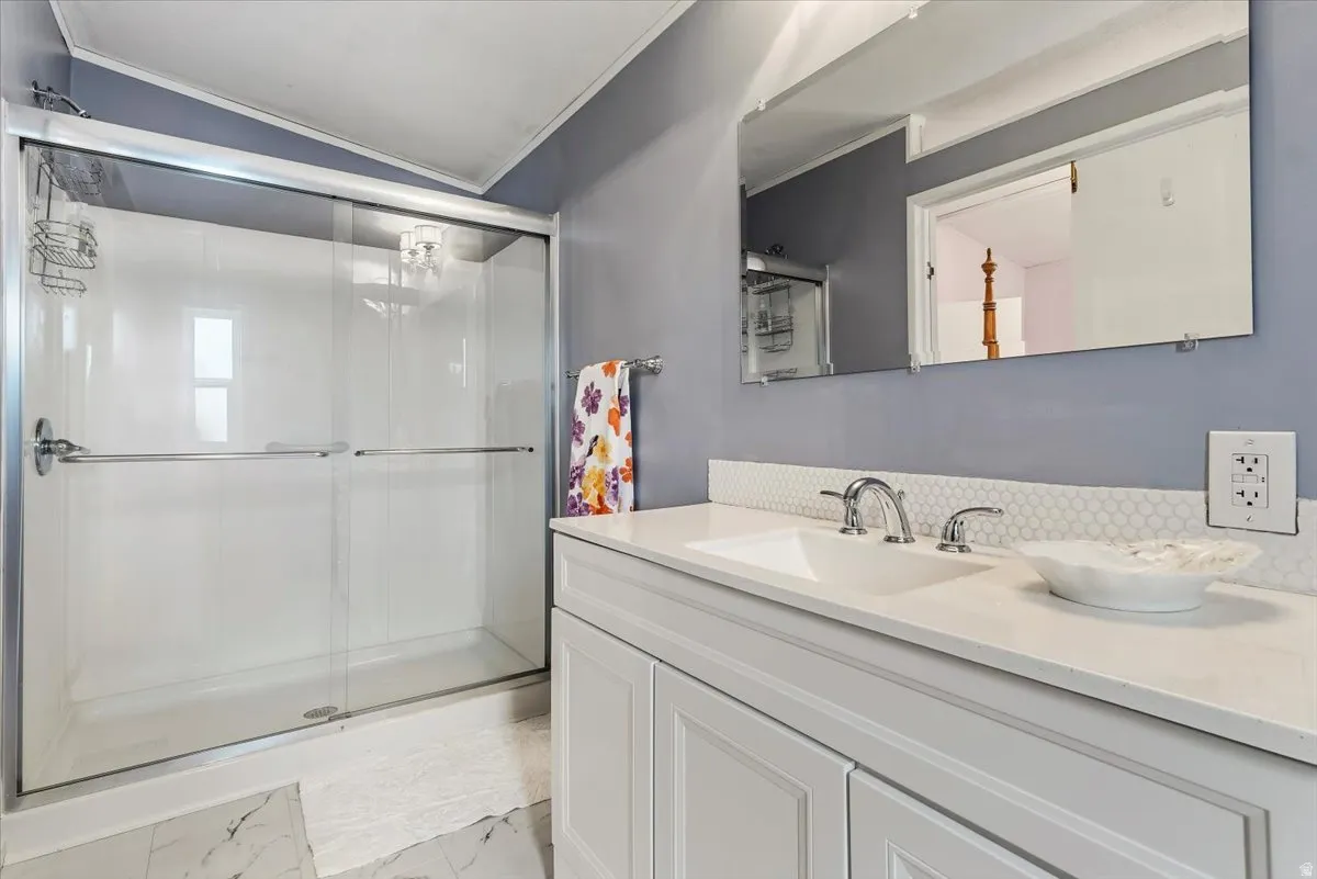 Bathroom featuring vanity, crown molding, a stall shower, light marble finish floors, and vaulted ceiling