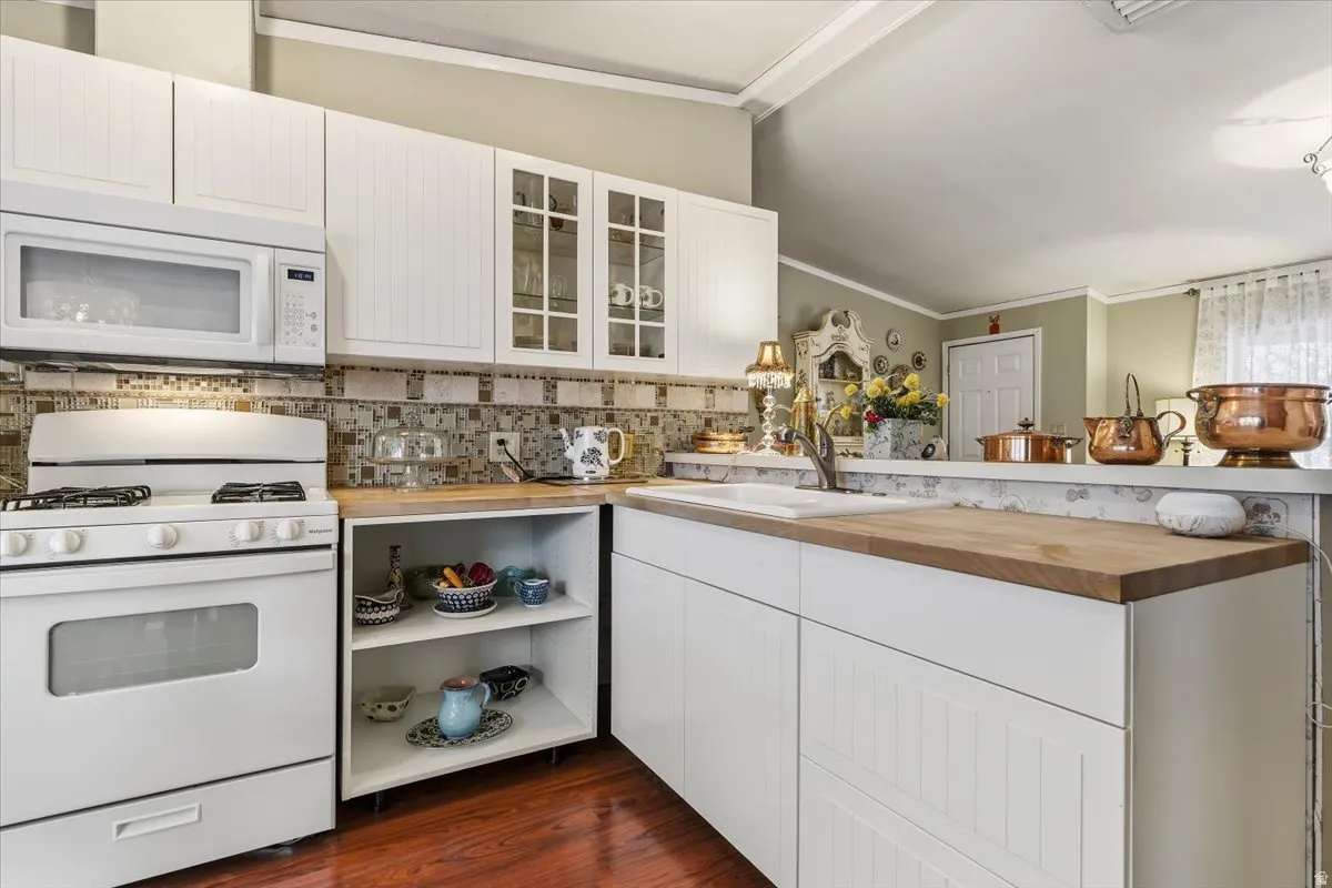 Kitchen featuring white appliances, gas range, butcher block countertops, white cabinetry, glass insert cabinets, and vaulted ceiling