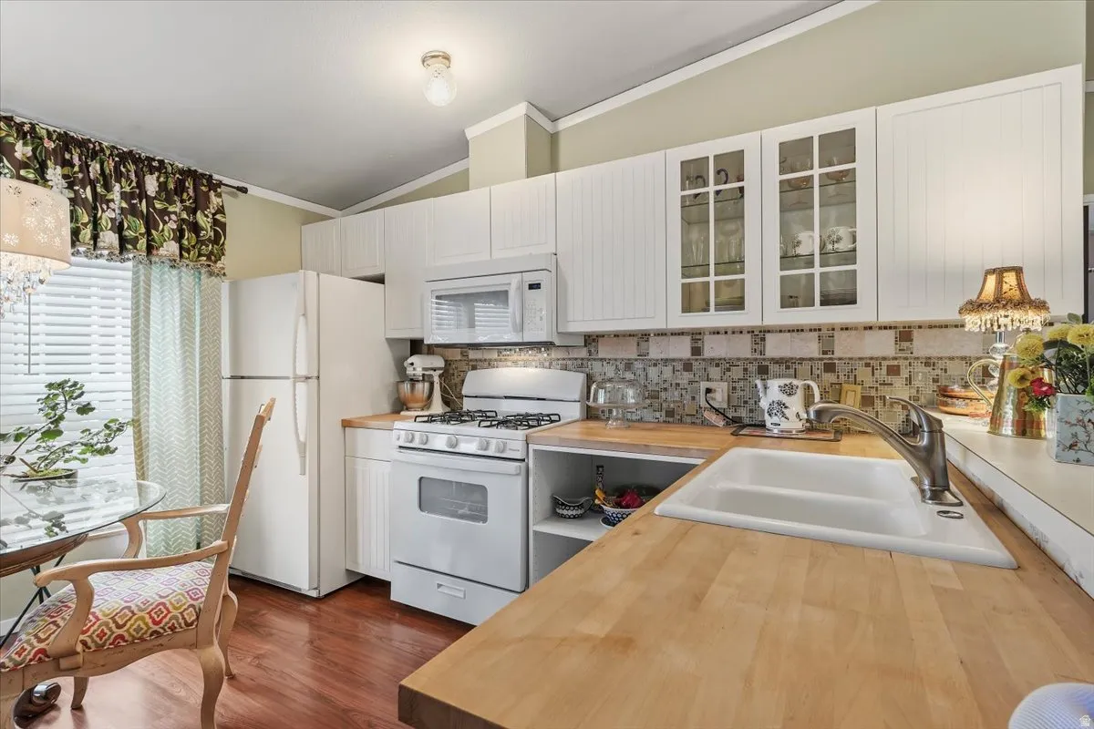 Kitchen featuring white appliances, vaulted ceiling, ornamental molding, tasteful backsplash, and glass fronted cabinets
