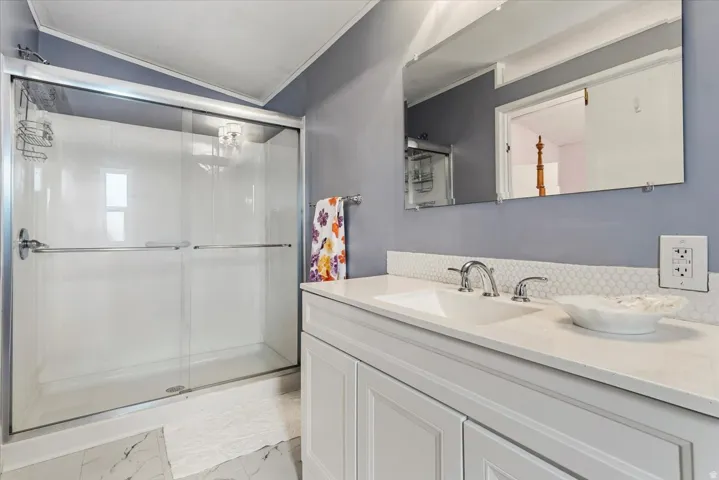 Bathroom featuring vanity, crown molding, a stall shower, light marble finish floors, and vaulted ceiling