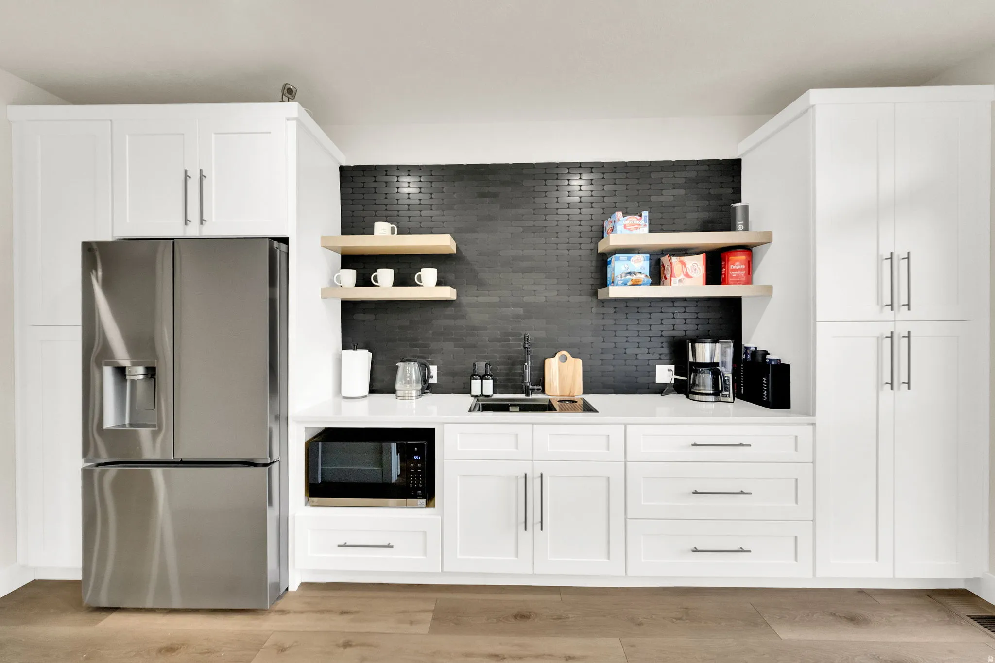 Kitchen featuring stainless steel fridge with ice dispenser, open shelves, white cabinets, black microwave, and backsplash