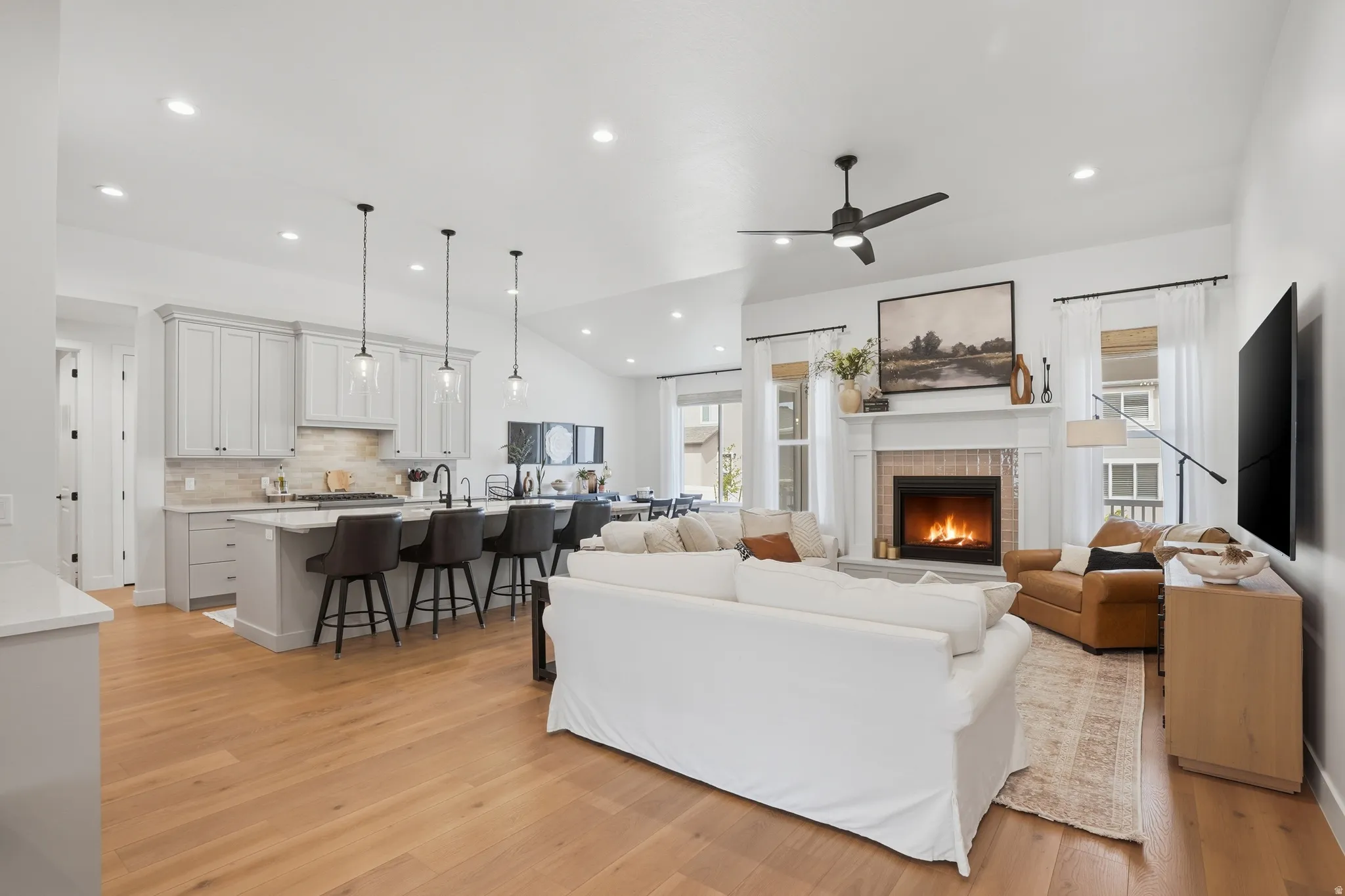 Living area with vaulted ceiling, a fireplace, a ceiling fan, light wood finished floors, and recessed lighting