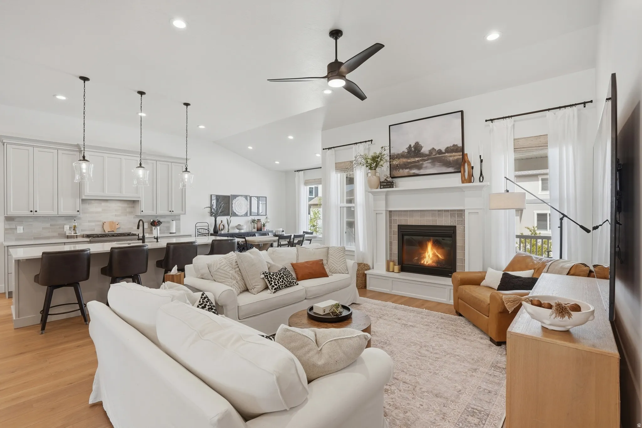 Living room with vaulted ceiling, a fireplace, ceiling fan, light wood-style floors, and recessed lighting