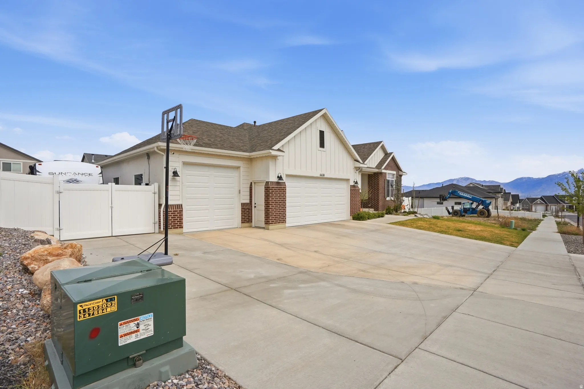 View of side of property featuring brick siding, board and batten siding, a gate, driveway, and an attached garage
