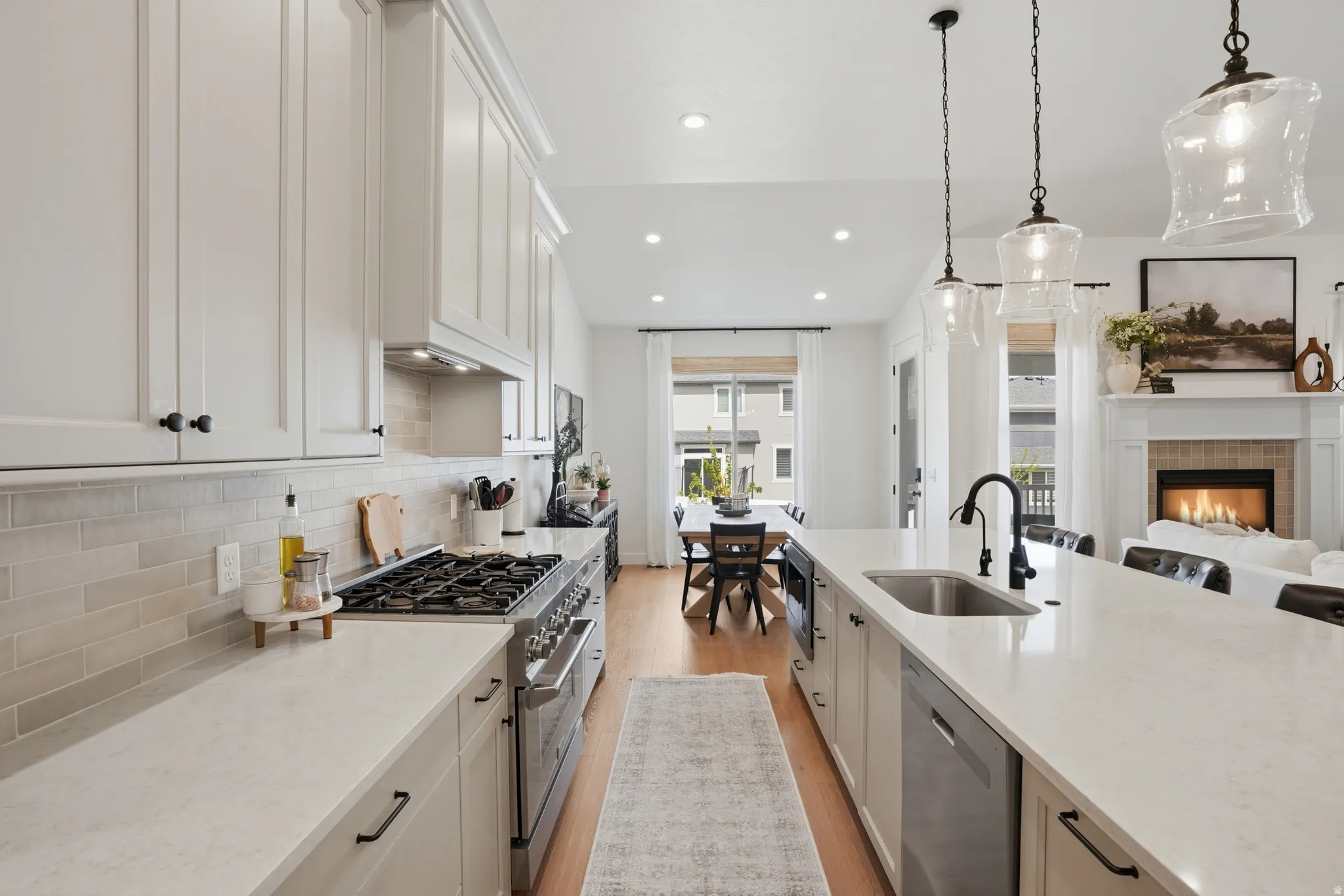 Kitchen with stainless steel appliances, a warm lit fireplace, white cabinetry, light wood finished floors, and light stone countertops