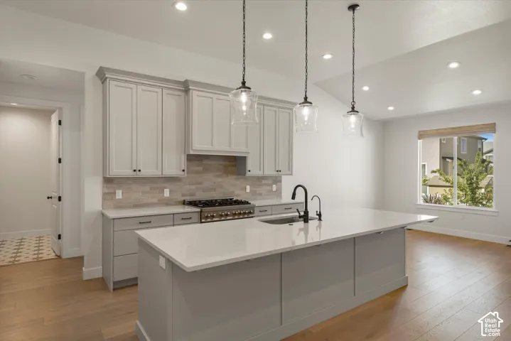 Kitchen featuring a gas range, light gray cabinetry, a large center island with an undermount sink, recessed lighting, and wood-finish flooring