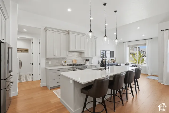 Kitchen with freestanding refrigerator, a kitchen bar, an island with sink, light wood-style floors, and vaulted ceiling