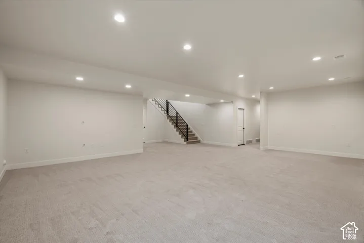 Expansive carpeted area with recessed lighting, a staircase featuring a metal railing, and white walls