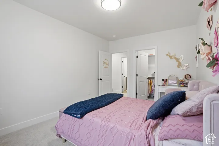 Bedroom with light colored carpet and a walk in closet