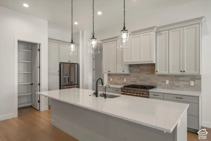 Kitchen featuring a large center island with a sink, stainless steel appliances, paneled cabinetry, a range with a tile backsplash, and recessed lighting