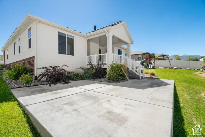 Rear exterior featuring a covered porch, white railing, and a ground-level concrete patio