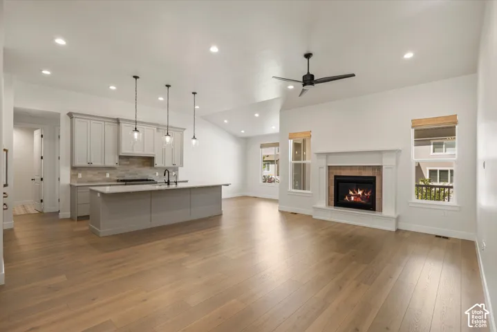 Vaulted ceiling, recessed lighting, wood-finish flooring, kitchen island with pendant lighting, and a fireplace with a mantel