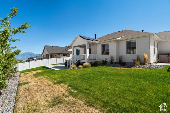 Expansive backyard featuring a manicured lawn, concrete patio, white vinyl fencing, and a covered porch