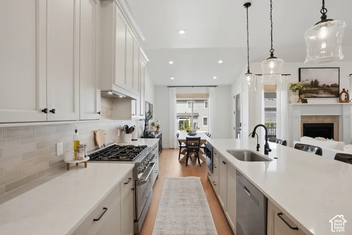 Kitchen with stainless steel appliances, white cabinets, a fireplace, light wood-type flooring, and light stone counters