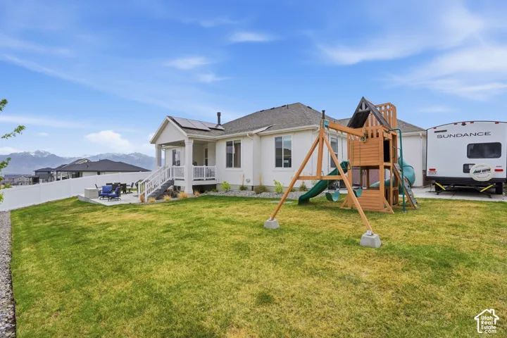 Rear view of property featuring a patio area, roof mounted solar panels, a playground, a mountain view, and stucco siding