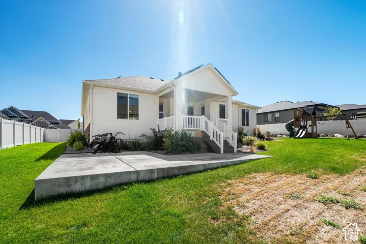 Rear exterior with a covered porch, concrete patio, and a manicured lawn