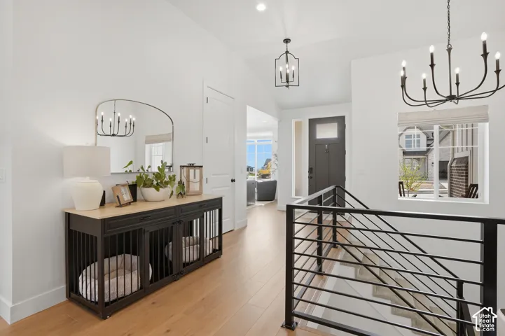 Corridor with suspended lighting, light wood-style flooring, an upstairs landing, and vaulted ceiling